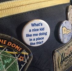 two badges on the back of a backpack that says, what's a nice kid like me doing in a place like this?