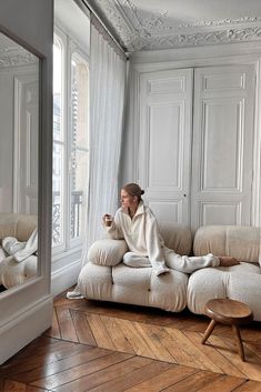 a woman sitting on top of a white couch next to a coffee cup in front of a window