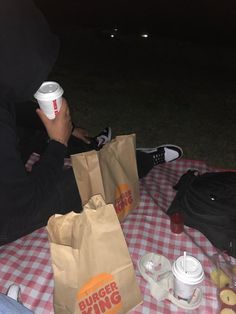 a person sitting at a picnic table with food and drinks