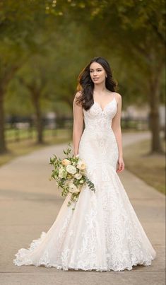 a woman in a wedding dress is standing on the sidewalk holding a bouquet and looking at the camera