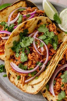 three tacos with shredded meat, onions and cilantro on a gray plate