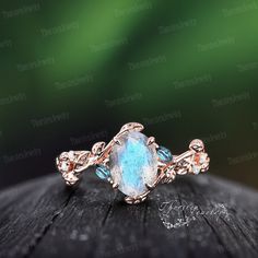 a blue stone ring sitting on top of a piece of wood with leaves around it