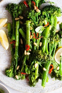 a white plate topped with broccoli covered in lemon wedges and pine nuts