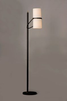 a black floor lamp with a white shade on it's side and a gray wall in the background