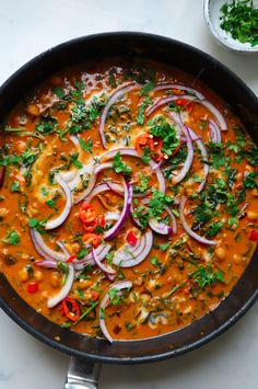 a skillet filled with red curry, onions and cilantro on top of a white table