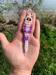 a hand is holding a small beaded keychain in front of the ocean