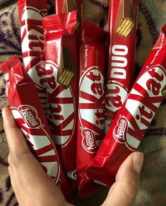 a person holding up a bunch of red and white candy bars with gold foil on them