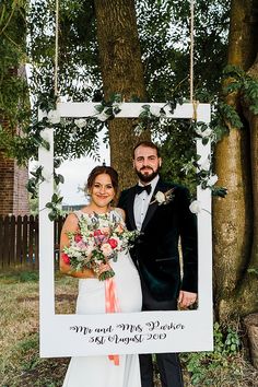 a man and woman standing next to each other in front of a white frame with greenery