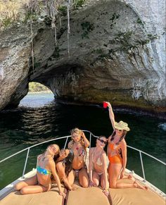 three women in bikinis sitting on the back of a boat with an arch above them