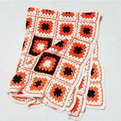 an orange and black crocheted afghan is laying on a white surface with three squares in the center