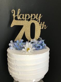 a white cake with blue flowers and a gold happy 70th birthday sign on the top