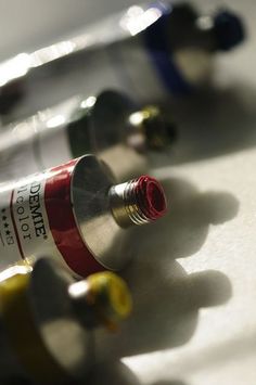 two wine bottles sitting next to each other on top of a white counter with yellow and red caps