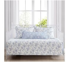 a white daybed with blue and white floral print on it in front of a window