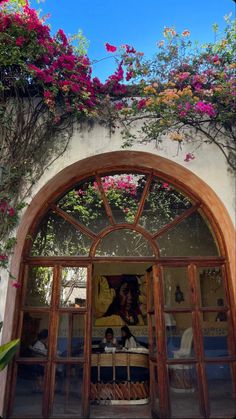 an arched doorway with flowers growing on the wall and below it is a painting of a woman