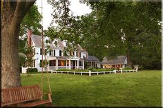 a large white house sitting on top of a lush green field next to a tree