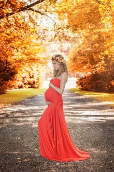 a pregnant woman in an orange dress standing on a road with trees and leaves around her