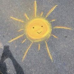 a smiley face drawn on the pavement with yellow chalk pastel and black crayons