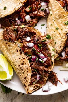 shredded beef tacos on a plate with lime wedges