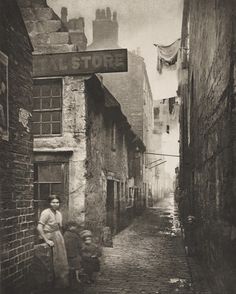 an old black and white photo of people walking down a narrow alleyway between two buildings