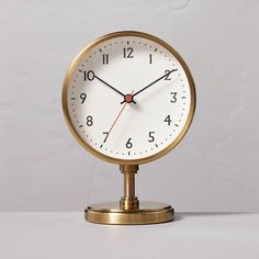 a gold clock on a white surface with numbers in the middle and one at the top