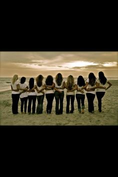 a group of women standing next to each other on top of a sandy beach with the ocean in the background