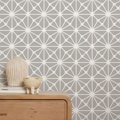 a white vase sitting on top of a wooden dresser next to a wall with geometric designs