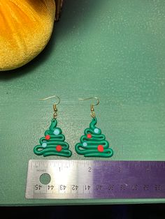 a pair of green christmas tree earrings sitting next to a ruler