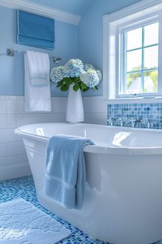 a white bath tub sitting under a window next to a blue and white tiled floor