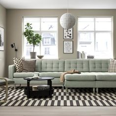 a living room with a checkered rug and large windows in the corner, along with a green couch