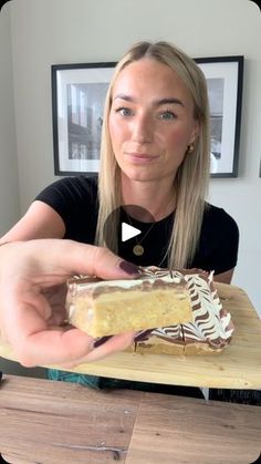 a woman holding a piece of cake on top of a wooden cutting board in front of her face