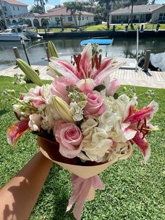 a bouquet of pink and white flowers sitting on top of a lush green field next to a body of water