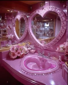 a pink bathroom with heart shaped mirrors and flowers on the counter top, along with two sinks