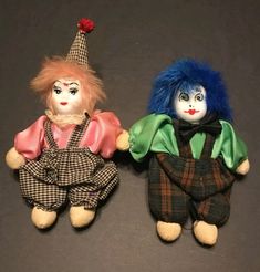 two dolls are sitting next to each other on a table with one doll wearing a clown's hat