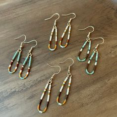 four pairs of earrings with beads on them sitting on top of a wooden table next to a pair of scissors