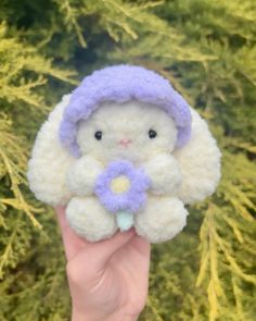 a hand holding a small stuffed animal with a flower in it's lap and wearing a purple hat