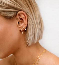 a woman with blonde hair is wearing gold ear cuffs and has two small diamond studs on her left ear