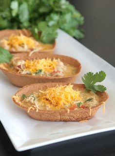 three baked potatoes with cheese and cilantro garnish on a white plate