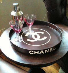 a chanel tray with two wine glasses on it sitting on a table next to a black cat