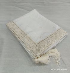 a white scarf with tassels is laying on a tablecloth that has been embroidered onto it