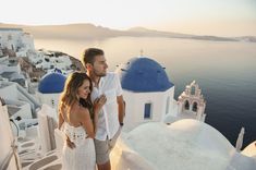 a man and woman standing on the edge of a building with blue domes in the background