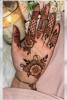 a woman's hand with henna tattoos on it and flowers in the background