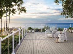 a deck with two chairs and a table on it next to the ocean at sunset