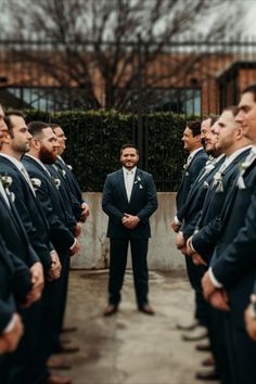 a group of men standing next to each other in front of a building and one man wearing a suit