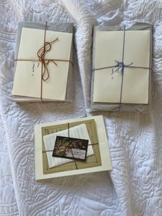 three wrapped gift boxes sitting on top of a white bed covered in sheets and twine