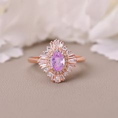 a close up of a ring with a pink stone in the center and white flowers behind it