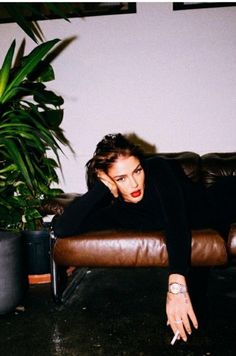 a woman sitting on top of a brown couch next to a potted plant