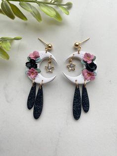 the moon and flower earrings are hanging from hooks on a white surface with green leaves