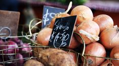 some onions are in a basket with a chalkboard sign attached to the top one