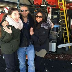 two women and a man are posing for a photo in front of a ski lift