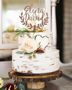 a white wedding cake with flowers on top sitting on a wooden stand in front of a mirror